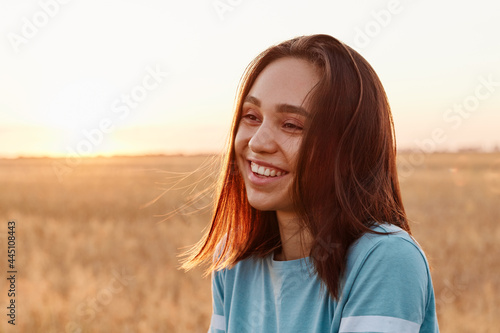 Summer portrait of laughing happy woman outdoor, enjoying warm sunshine, wearing blue t shirt, having dark hair, looking away with toothy smile, expressing happiness.