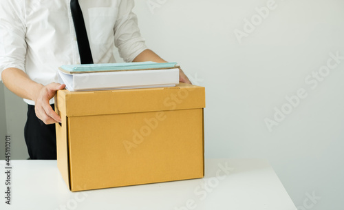 A man office worker is unhappy with being fired from a company packing things into cardboard boxes. The young man was stressed and disappointed by being fired. concept of layoffs and unemployment © Orathai