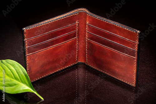 Leather brown open purse and green leaf on a dark background.
