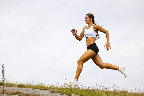 Determined Fit Female Athlete Running On Mountain Against Sky