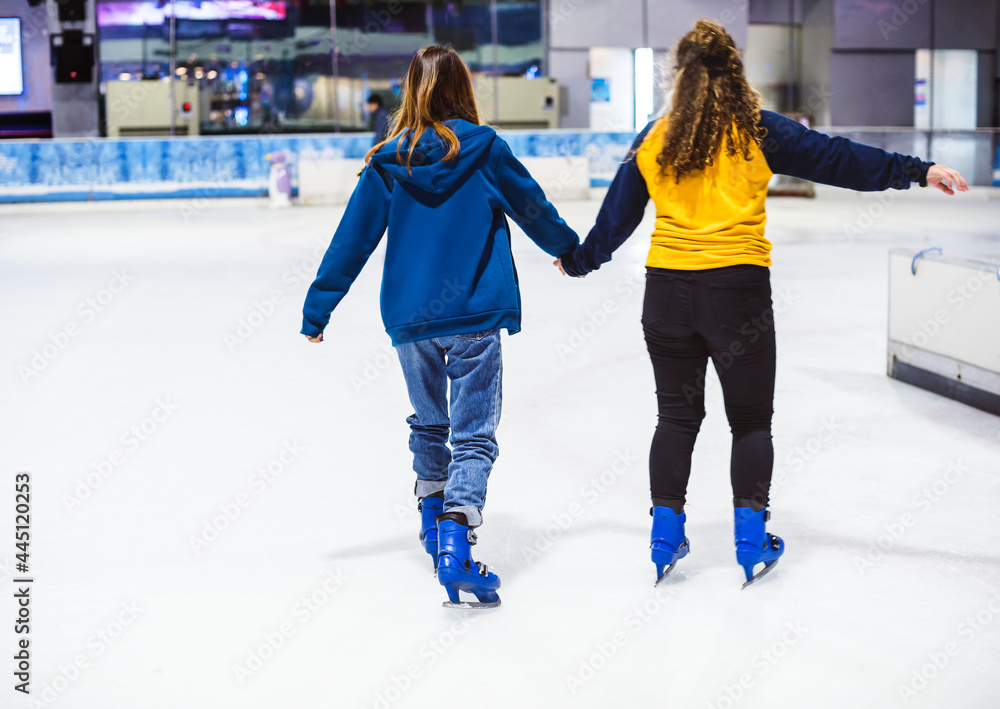 Girl friends ice skating on the ice rink together - obrazy, fototapety, plakaty 