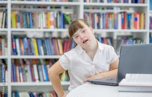 Portrait of a smiling girl with syndrome down using a laptop at library. Education for disabled children concept