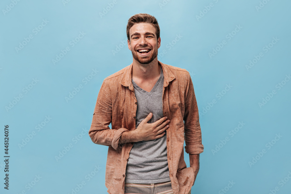 © Look! - Joyful fashionable man with ginger beard in grey t-shirt and stylish shirt laughing and posing on isolated blue background..