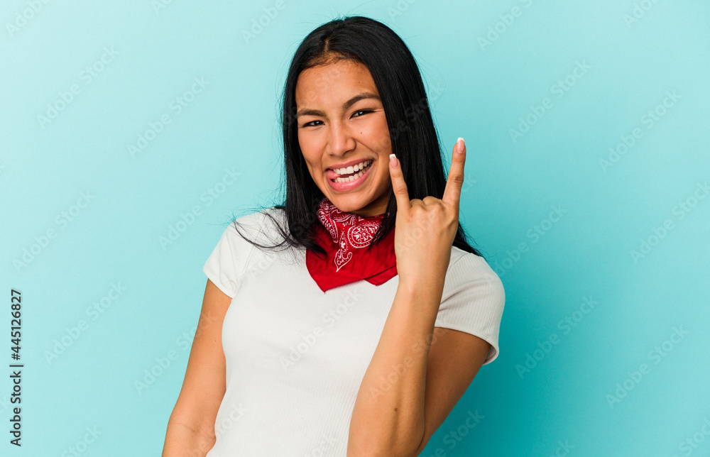 Young Venezuelan woman isolated on blue background showing rock gesture with fingers Young Venezuelan woman isolated on blue background showing rock gesture with fingers