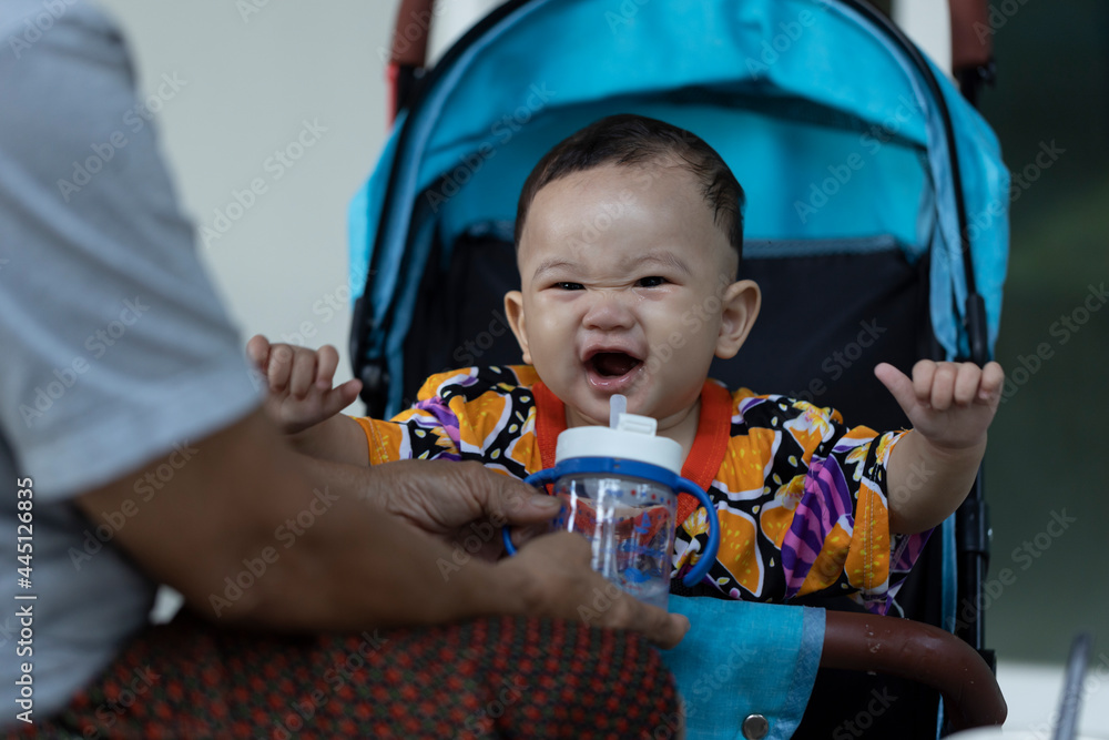 Cute 8 month old boy sitting on a blue stroller about to drink from a water bottle and laugh. Baby is drink water from bottle. Baby is laughing. Cute 8 month old boy sitting on a blue stroller about to drink from a water bottle and laugh. Baby is drink water from bottle. Baby is laughing.