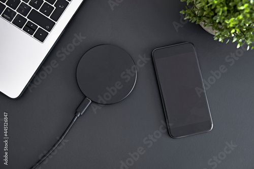 Recharging smartphone battery using round induction wireless charger. Top down view of office workplace. photo