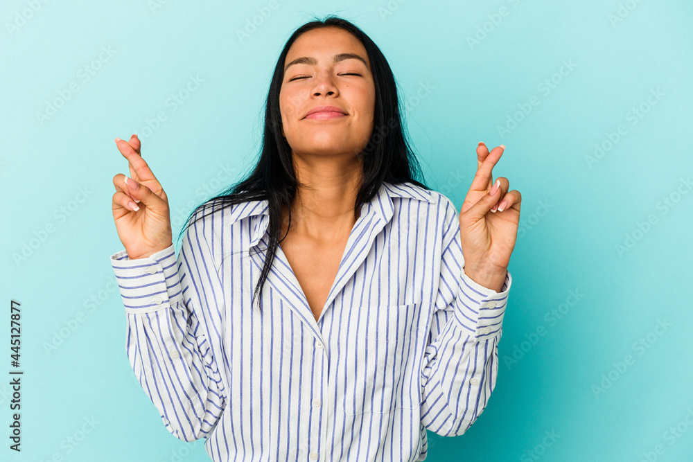 Young Venezuelan woman isolated on blue background crossing fingers for having luck Young Venezuelan woman isolated on blue background crossing fingers for having luck