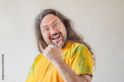 The man happily shows a thumb up. A casually and sloppy dressed man with a beard and long hair in a paint-stained T-shirt on a light background. photo