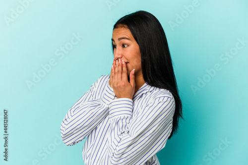 Young Venezuelan woman isolated on blue background laughing about something, covering mouth with hands.