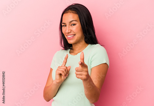 Young Venezuelan woman isolated on pink background pointing to front with fingers.