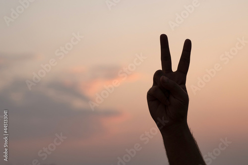 Man creating the peace symbol with his hand against the evening sky - silhouette