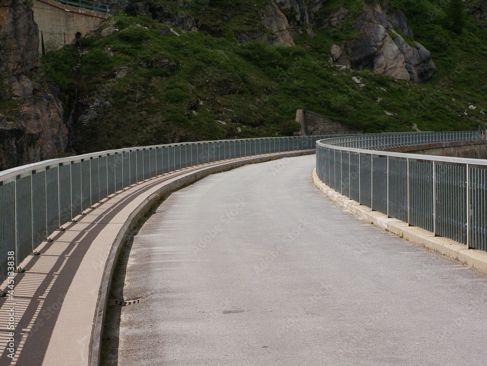 single lane road with railings at the roadside, in a curve. Road on the embankment dam at Lac de Moiry, Switzerland single lane road with railings at the roadside, in a curve. Road on the embankment dam at Lac de Moiry, Switzerland
