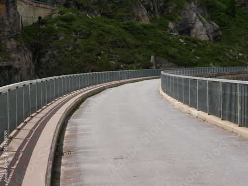 single lane road with railings at the roadside, in a curve. Road on the embankment dam at Lac de Moiry, Switzerland