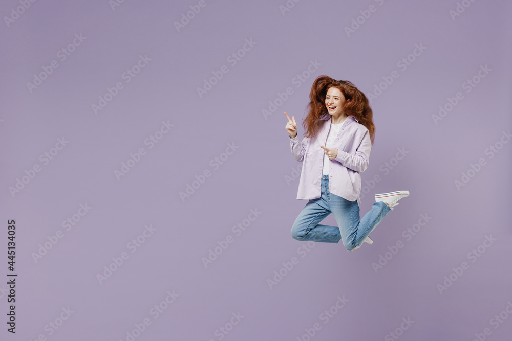 Full size young redhead curly woman 20s wears white T-shirt violet jacket jump pointing on workspace area copy space mock up look aside isolated on pastel purple color wall background studio portrait. Full size young redhead curly woman 20s wears white T-shirt violet jacket jump pointing on workspace area copy space mock up look aside isolated on pastel purple color wall background studio portrait.
