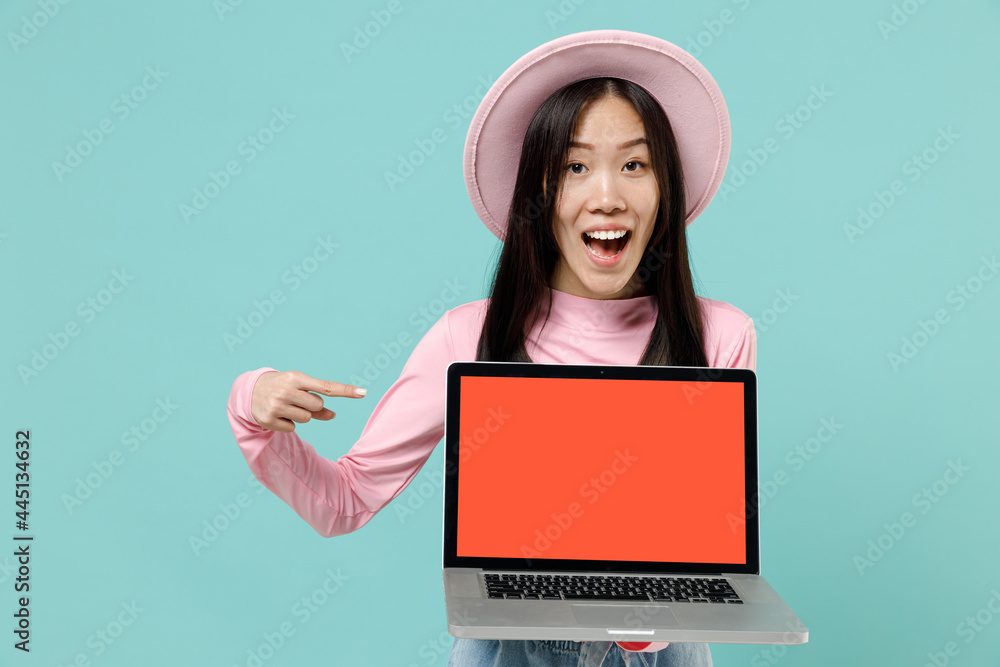 Amazed fun young brunette asian woman 20s wears pink clothes hold use work on laptop pc computer with blank screen workspace area point on it isolated on pastel blue color background studio portrait Amazed fun young brunette asian woman 20s wears pink clothes hold use work on laptop pc computer with blank screen workspace area point on it isolated on pastel blue color background studio portrait