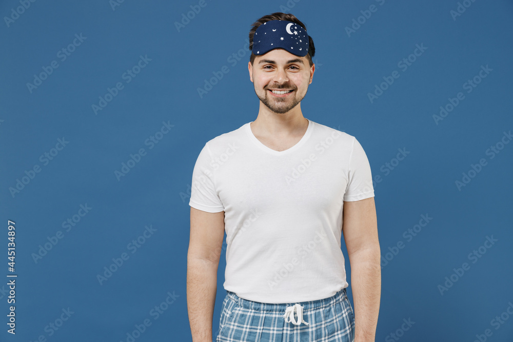 Calm smiling caucasian happy fun young man 20s wearing pajamas jam sleep mask white t-shirt resting relaxing at home looking camera isolated on dark blue background Good mood night bedtime concept Calm smiling caucasian happy fun young man 20s wearing pajamas jam sleep mask white t-shirt resting relaxing at home looking camera isolated on dark blue background Good mood night bedtime concept