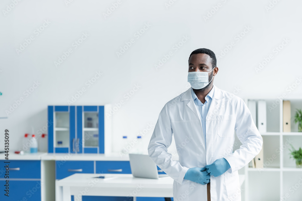 African american scientist in medical mask adjusting white coat in lab African american scientist in medical mask adjusting white coat in lab