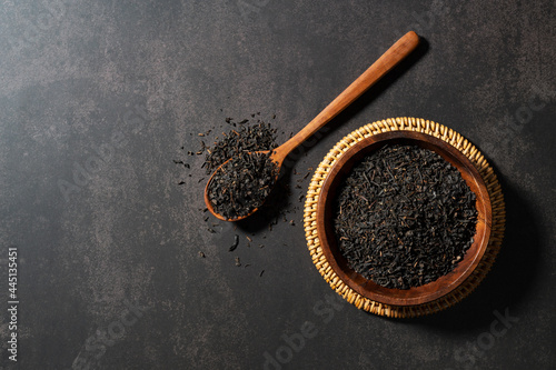Tea leaves in a spoon with a wooden plate on a black background