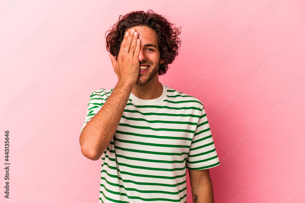 Young caucasian man isolated on pink bakcground having fun covering half of face with palm. Young caucasian man isolated on pink bakcground having fun covering half of face with palm.