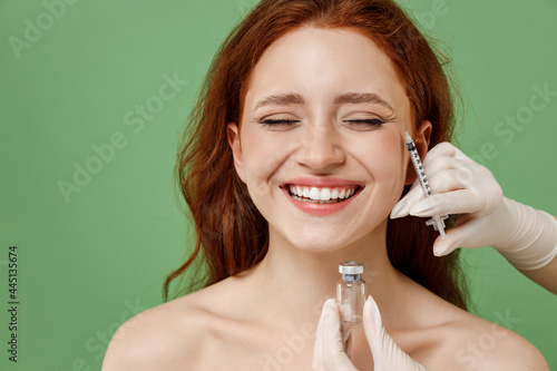Beautiful smiling half naked topless redhead woman nude make up visit doctor making mesotherapy injection isolated on pastel green color background. Skin care healthcare cosmetic procedures concept photo
