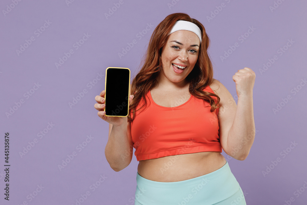 Young chubby plus size big fat woman in red top warm up training hold yoga mat mobile cell phone blank screen workspace do winner gesture isolated on purple background home gym Workout sport concept.
