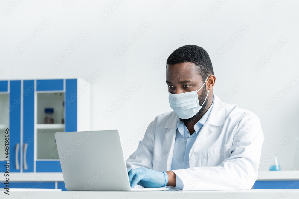 African american scientist in medical mask using laptop in laboratory African american scientist in medical mask using laptop in laboratory