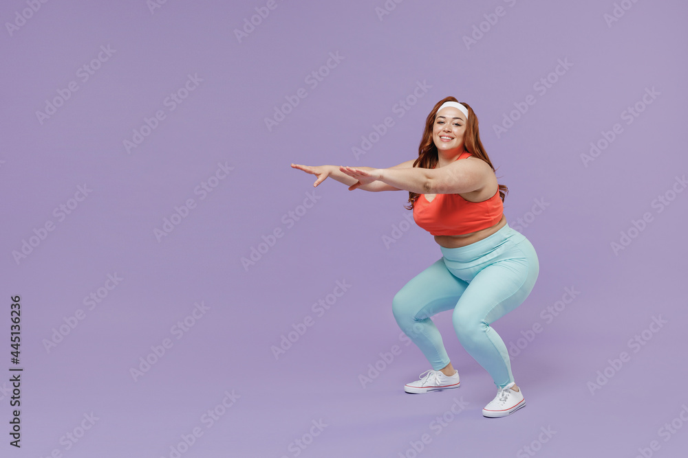 Full length side view fun young chubby overweight plus size big fat fit woman in red top warm up training squating look camera isolated on purple background home gym. Workout sport motivation concept. Full length side view fun young chubby overweight plus size big fat fit woman in red top warm up training squating look camera isolated on purple background home gym. Workout sport motivation concept.