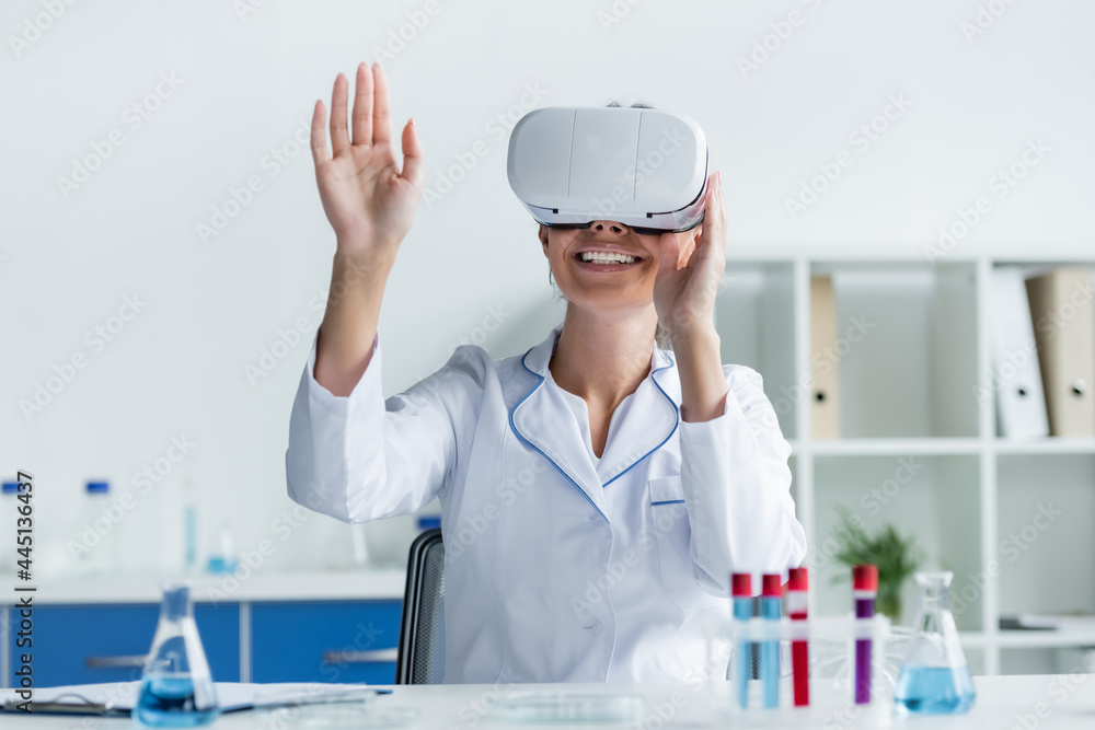 Smiling scientist in vr headset sitting near test tubes on blurred foreground Smiling scientist in vr headset sitting near test tubes on blurred foreground