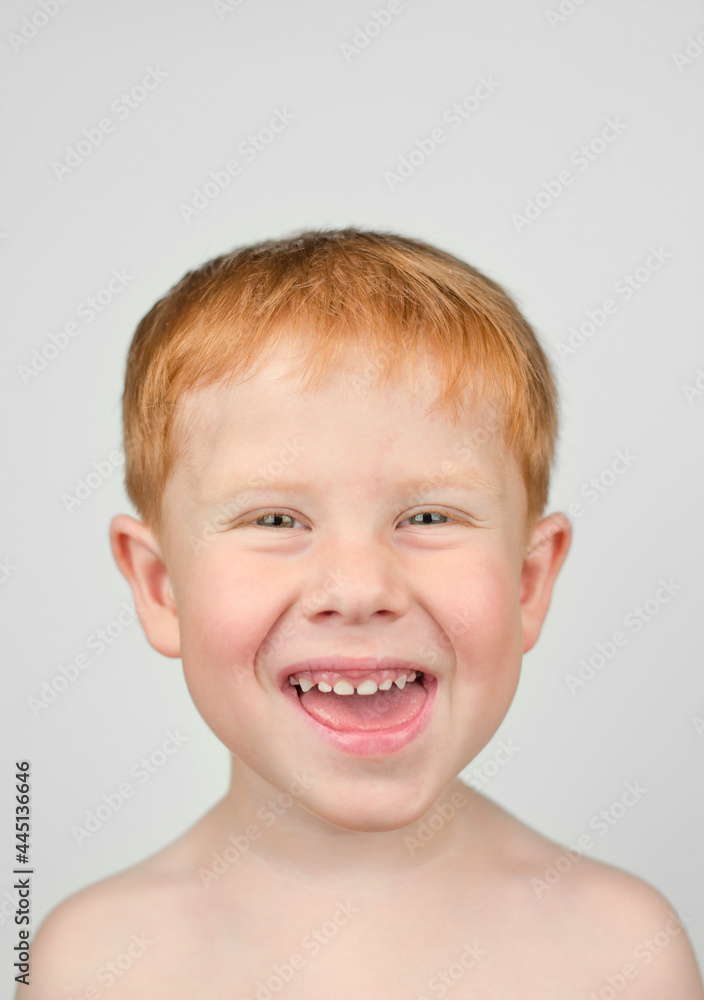 Close up portrait of 4 year old redhead boy. The boy looks at the camera and laughs on a gray background. Happy child Close up portrait of 4 year old redhead boy. The boy looks at the camera and laughs on a gray background. Happy child