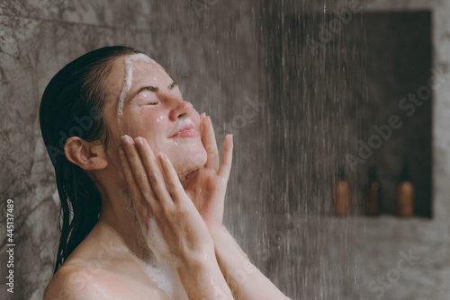 Tablou pe pânză Side view amazed half naked topless young woman 20s taking cold and hot shower rinse foam stand under water in bathroom in brown background
