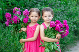 Girls in pink dresses with bouquets of peonies in the countryside
