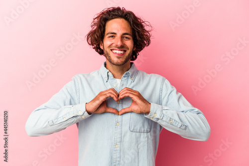 Young caucasian man isolated on pink bakcground smiling and showing a heart shape with hands. photo