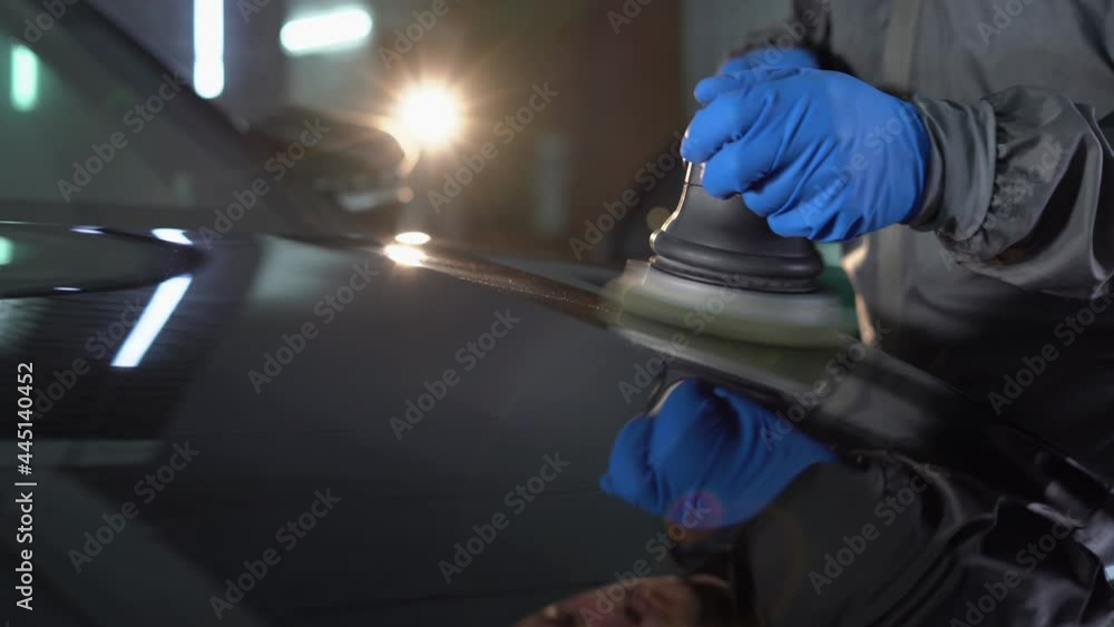 Close-up of a male worker's hand he polishes the car body with a grinder and wax from scratches at a car service. Close-up of a male worker's hand he polishes the car body with a grinder and wax from scratches at a car service.