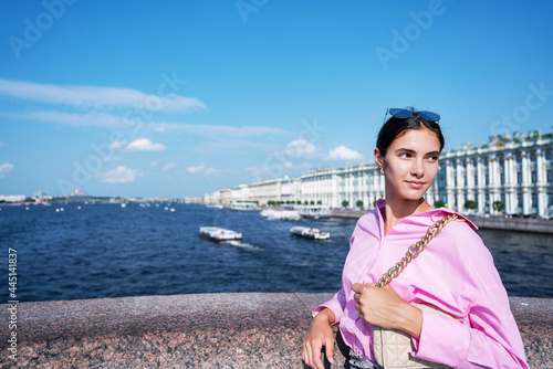 Pretty young lady wearing pink shirt with beige handbag standing at city street