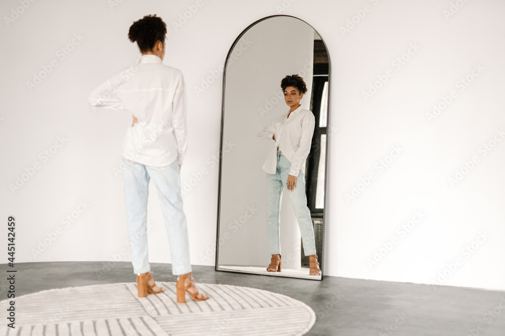 Young black woman standing and looking at mirror indoors - obrazy, fototapety, plakaty 