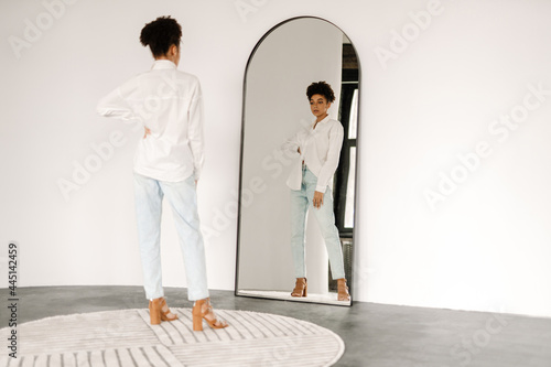Young black woman standing and looking at mirror indoors photo