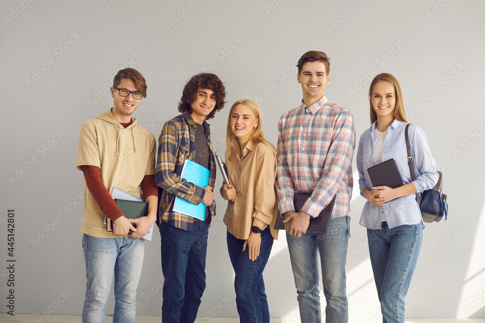 Obraz premium Positive happily smiling male and female teenage students group portrait isolated on grey copy space background. Stylish good-looking young people with studying stationary full length studio shot