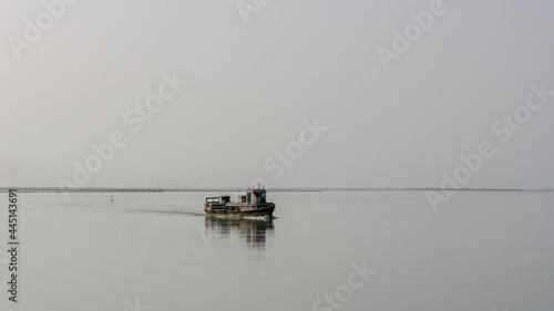 Minimalist landscape view of small wooden ferry boat crossing the mighty Brahmaputra river in Assam, India