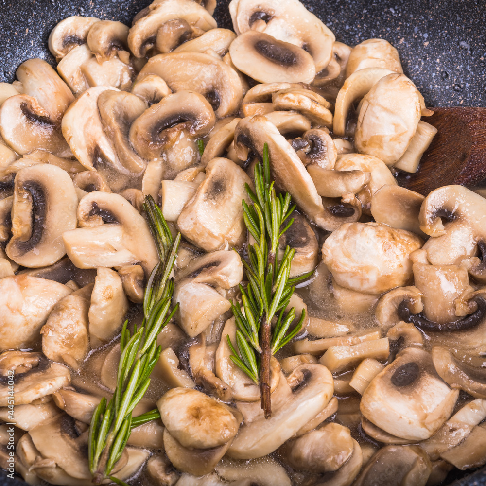 Mushrooms are fried with rosemary - sliced champignons in a pan close-up Mushrooms are fried with rosemary - sliced champignons in a pan close-up