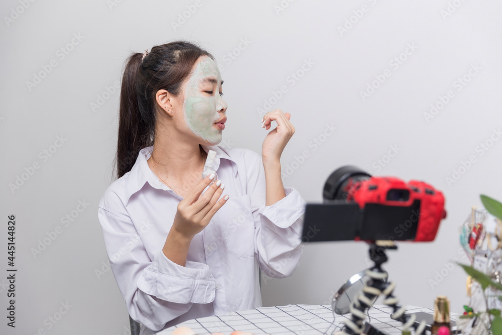 blogging, technology, videoblog, makeup and people concept - happy smiling woman or beauty blogger with bronzerwith face mask polishing nails and camera recording tutorial video blogging, technology, videoblog, makeup and people concept - happy smiling woman or beauty blogger with bronzerwith face mask polishing nails and camera recording tutorial video