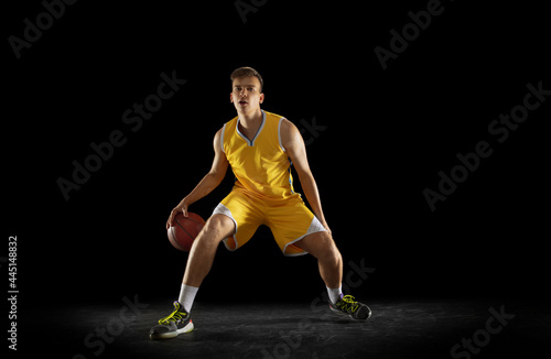 Basketball player with a ball in action and motion isolated on dark black studio background. Advertising concept. Strong Caucasian athlete practicing with basketball ball.