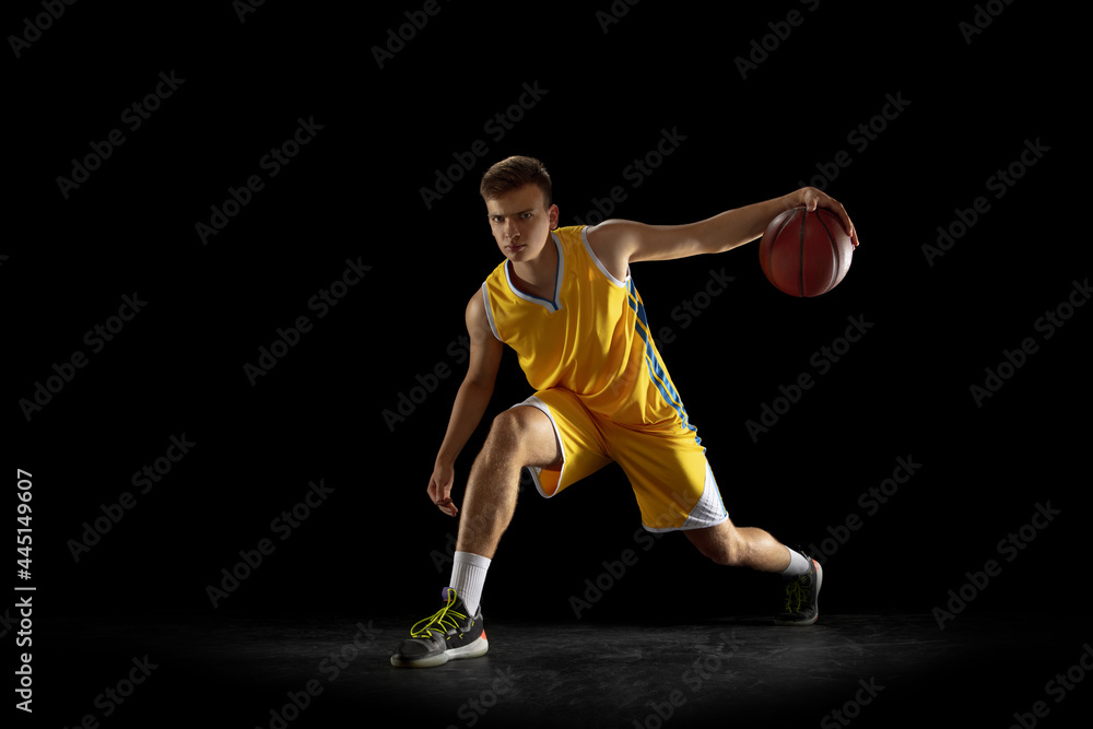 Basketball player with a ball training isolated on dark black studio background. Advertising concept. Fit Caucasian athlete practicing with ball.