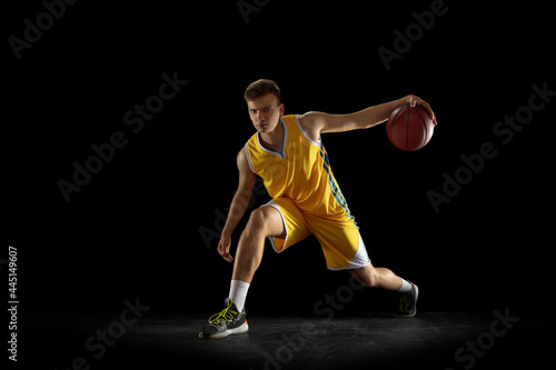 Basketball player with a ball training isolated on dark black studio background. Advertising concept. Fit Caucasian athlete practicing with ball. © master1305