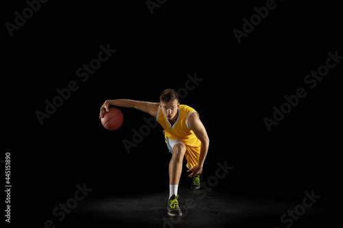 Basketball player with a ball training isolated on dark black studio background. Advertising concept. Fit Caucasian athlete practicing with ball.