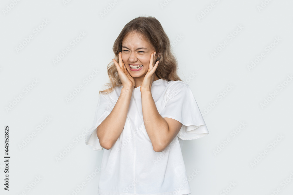 Charming woman is smiling touching her cheeks posing in a white t-shirt on a studio wall Charming woman is smiling touching her cheeks posing in a white t-shirt on a studio wall