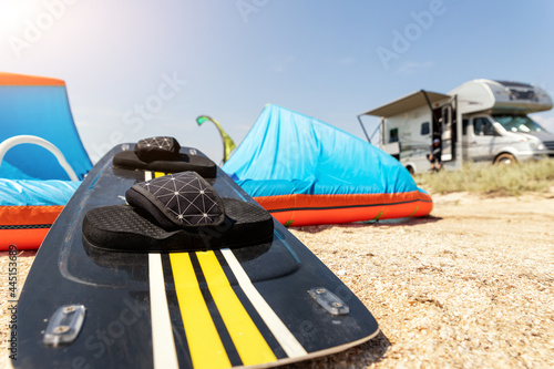 Close-up surf board and kite equipment on sand beach shore watersport spot on bright sunny day against rv camper van vehicle at sea ocean coast at surfing camp. Fun adventure travel sport acitivity