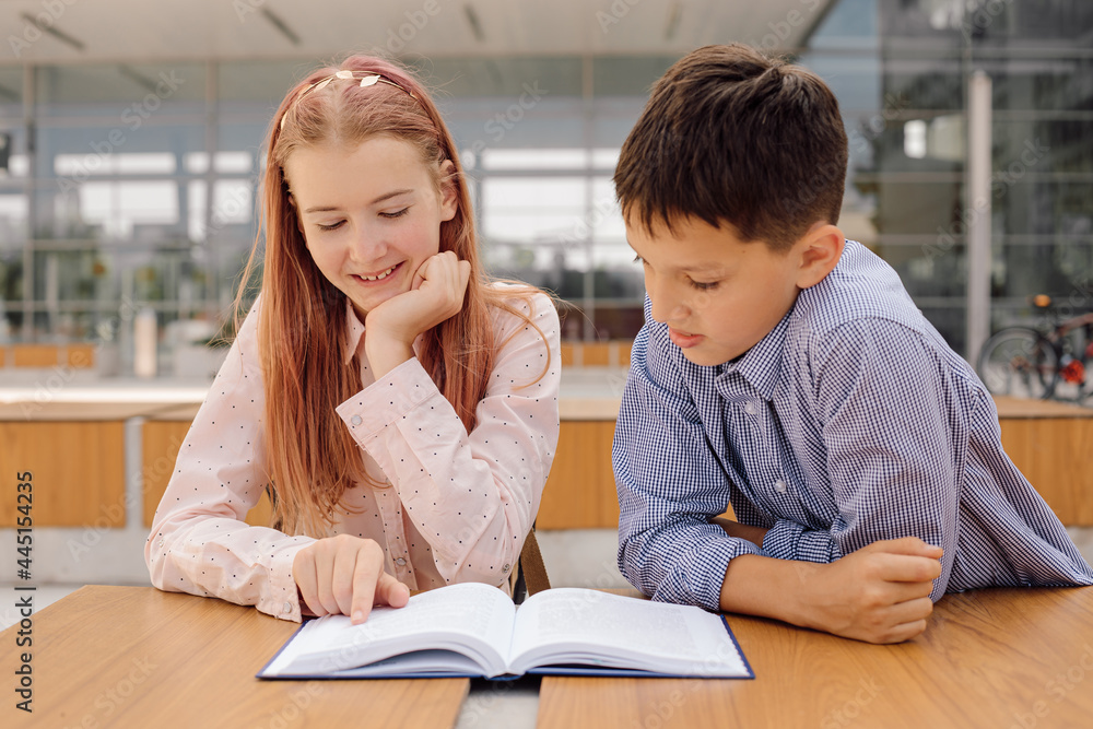 Primary secondary education, school, concept of friendship - two students boy and teenage girl with backpacks are sitting, talking after school with book and bug Primary secondary education, school, concept of friendship - two students boy and teenage girl with backpacks are sitting, talking after school with book and bug