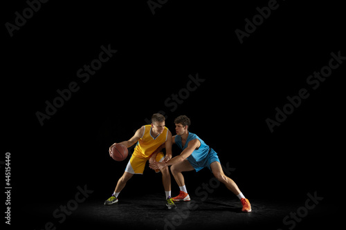 Two basketball players in action and motion isolated on dark black studio background. Advertising concept. Strong Caucasian athletes practicing with basketball ball. © master1305