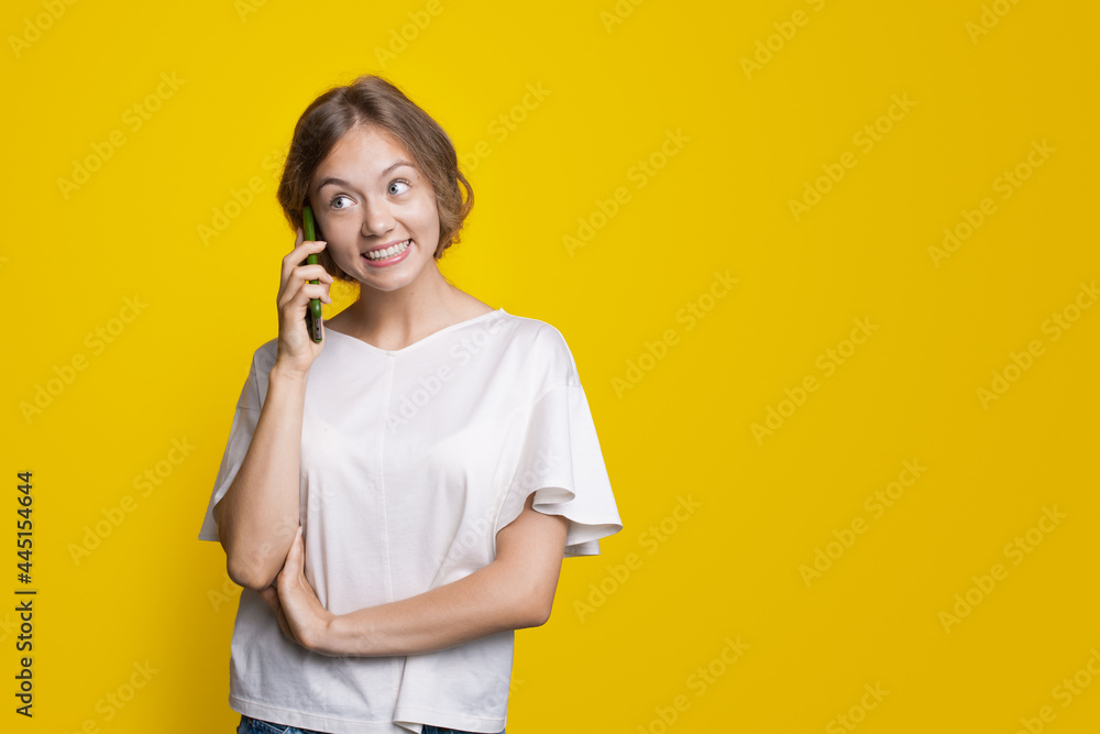 Adorable blonde lady is talking on phone smiling on a yellow studio wall near free space Adorable blonde lady is talking on phone smiling on a yellow studio wall near free space