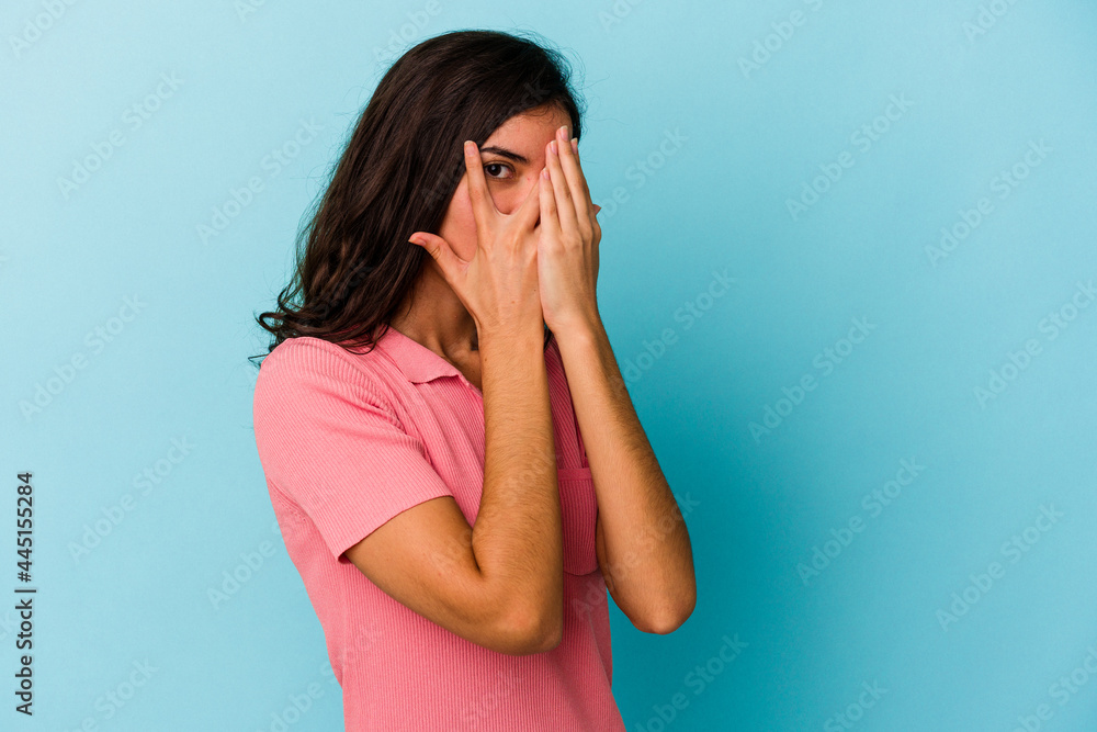 Young caucasian woman isolated on blue background blink through fingers frightened and nervous. Young caucasian woman isolated on blue background blink through fingers frightened and nervous.